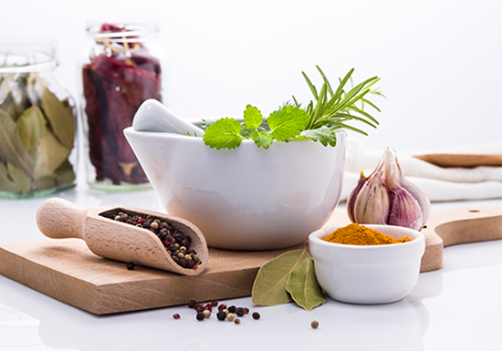 Tagliere di legno con una selezione di alimenti sani e naturali per la longevità: noci, semi vari, erbe aromatiche fresche, spicchi d'aglio e cereali.