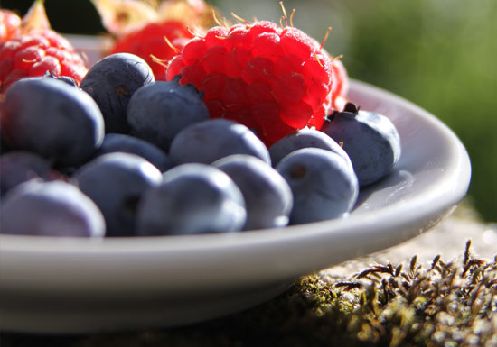 Vassoio di legno ricolmo di lamponi rossi e mirtilli blu freschi, rappresentazione di alimenti ricchi di antiossidanti naturali per la salute cellulare.